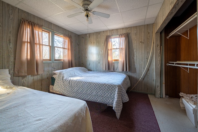 bedroom with ceiling fan, wooden walls, and a drop ceiling