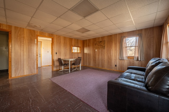 unfurnished living room featuring a paneled ceiling and wood walls