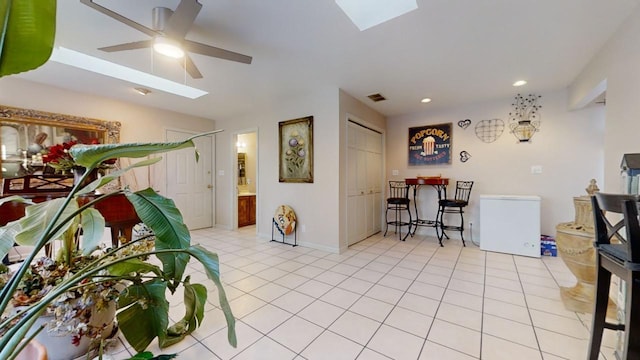 tiled living room with ceiling fan and a skylight