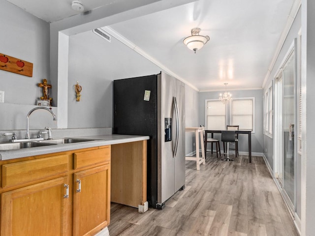 kitchen with a notable chandelier, light hardwood / wood-style floors, sink, ornamental molding, and stainless steel fridge