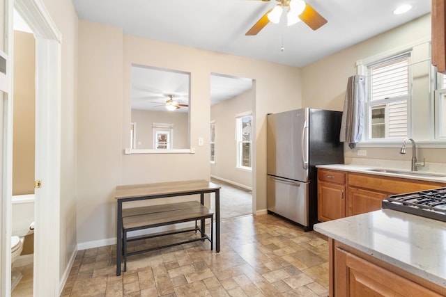 kitchen with ceiling fan, light stone counters, sink, and stainless steel refrigerator