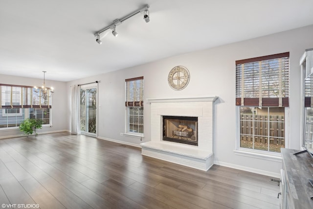 unfurnished living room featuring an inviting chandelier, a fireplace, a wealth of natural light, and track lighting