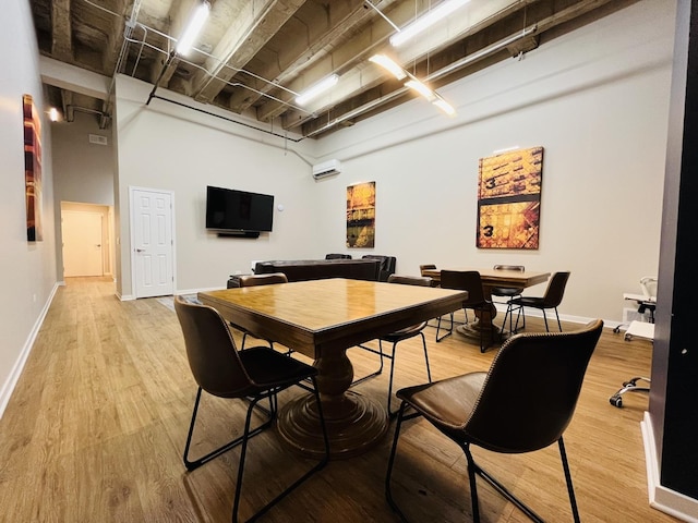 dining area with light hardwood / wood-style flooring, a wall unit AC, and a high ceiling