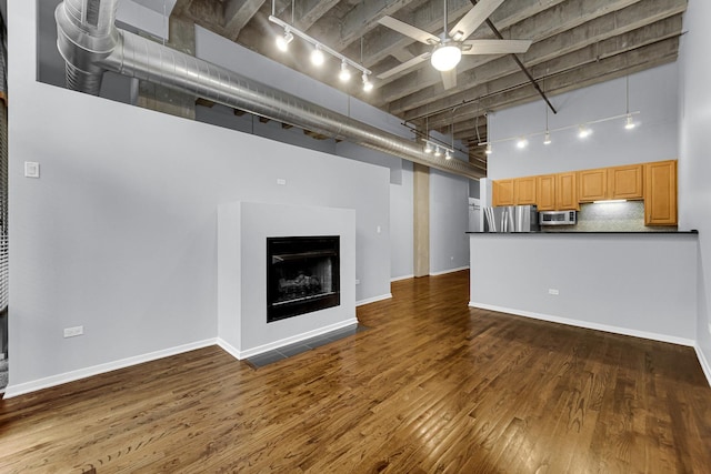 unfurnished living room featuring dark wood-type flooring, ceiling fan, rail lighting, and a high ceiling