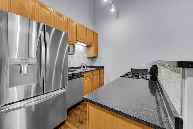 kitchen with sink, kitchen peninsula, hardwood / wood-style flooring, stainless steel appliances, and decorative backsplash