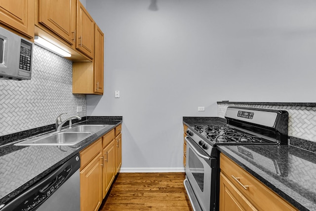 kitchen with sink, dark wood-type flooring, dark stone countertops, stainless steel appliances, and decorative backsplash