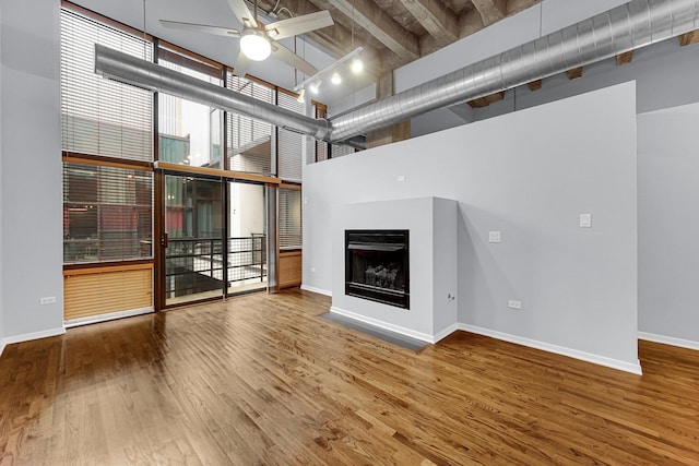 unfurnished living room featuring a towering ceiling, wood-type flooring, expansive windows, and ceiling fan