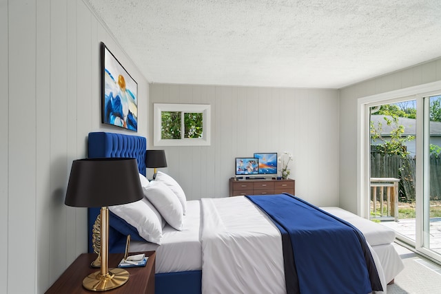 bedroom with wood walls, a textured ceiling, and access to outside