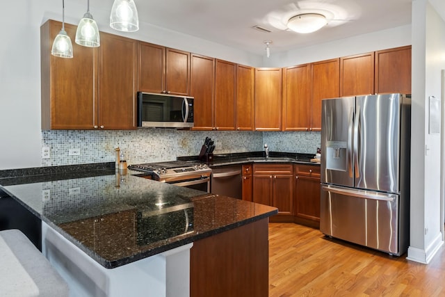 kitchen with appliances with stainless steel finishes, pendant lighting, dark stone counters, kitchen peninsula, and light hardwood / wood-style flooring