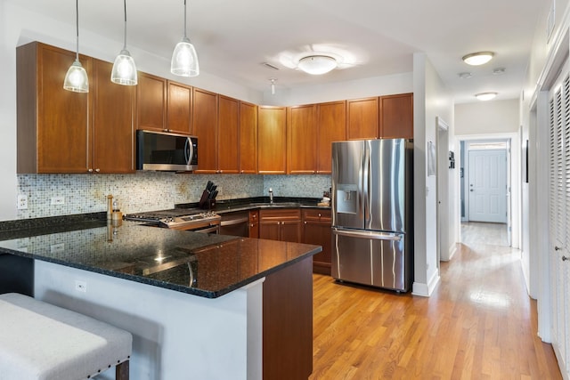 kitchen featuring stainless steel appliances, a kitchen breakfast bar, kitchen peninsula, and dark stone countertops