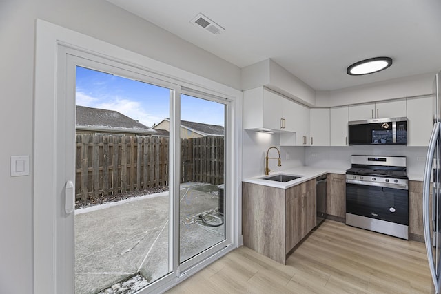 kitchen with appliances with stainless steel finishes, light wood-type flooring, white cabinets, and sink