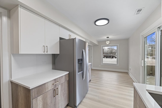 kitchen featuring stainless steel fridge, white cabinetry, light wood-type flooring, and hanging light fixtures