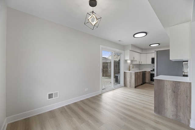 kitchen with sink, white cabinets, light wood-type flooring, stainless steel range, and pendant lighting