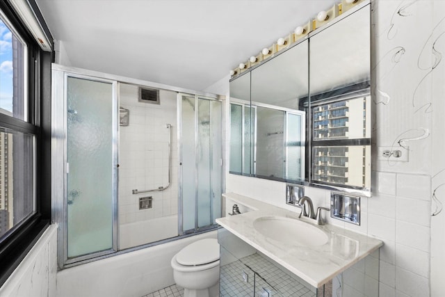 full bathroom featuring combined bath / shower with glass door, tile patterned floors, toilet, vanity, and tile walls