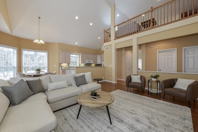 living room featuring a wealth of natural light, high vaulted ceiling, light hardwood / wood-style floors, and an inviting chandelier