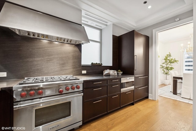 kitchen with dark brown cabinetry, exhaust hood, a notable chandelier, high quality appliances, and plenty of natural light