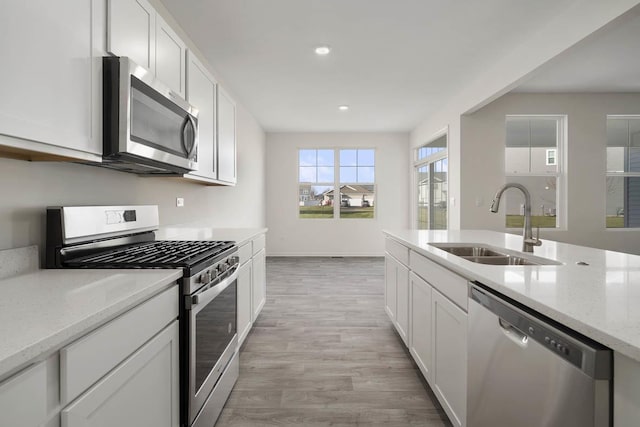 kitchen featuring sink, light stone countertops, light wood-type flooring, white cabinetry, and stainless steel appliances