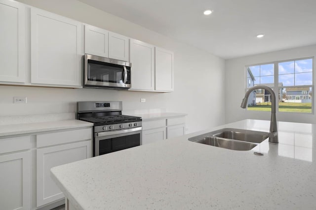 kitchen featuring white cabinets, stainless steel appliances, light stone counters, and sink