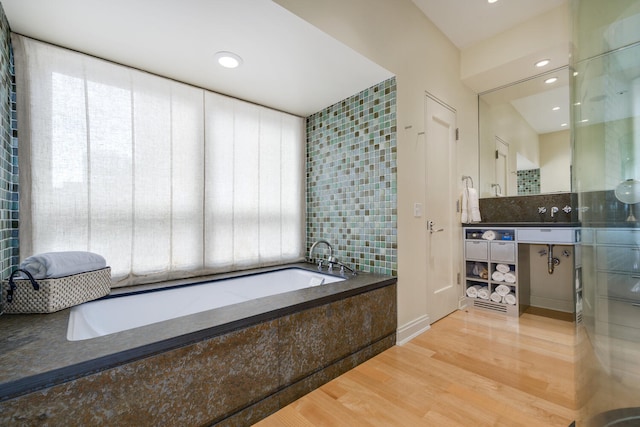 bathroom featuring decorative backsplash, a relaxing tiled tub, and hardwood / wood-style flooring