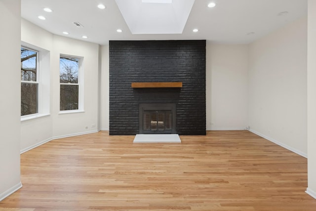 unfurnished living room with a skylight, a fireplace, and light wood-type flooring