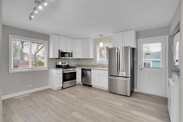 kitchen with appliances with stainless steel finishes, light wood-type flooring, white cabinetry, and pendant lighting