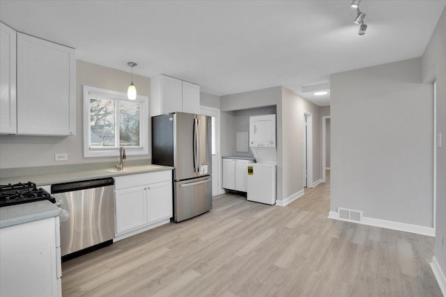 kitchen featuring appliances with stainless steel finishes, sink, decorative light fixtures, white cabinetry, and stacked washer / drying machine