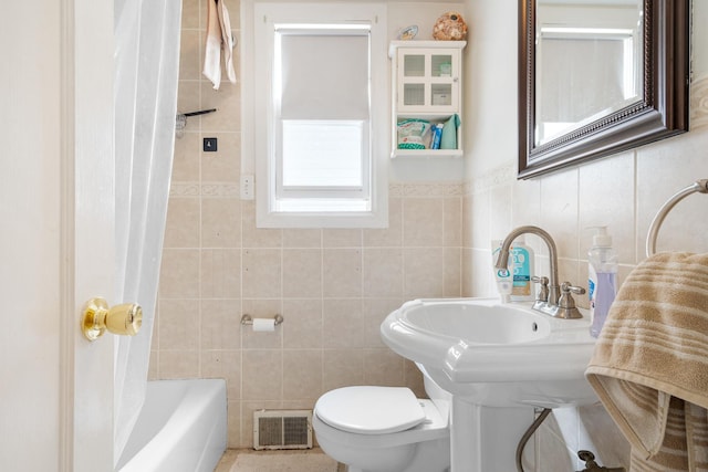 bathroom with toilet, tile walls, and shower / tub combo with curtain