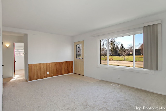 unfurnished room with wooden walls and light colored carpet