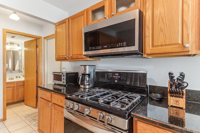 kitchen with light tile patterned flooring, sink, appliances with stainless steel finishes, and dark stone counters