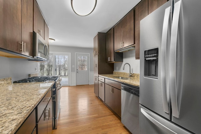 kitchen with sink, light hardwood / wood-style flooring, light stone countertops, appliances with stainless steel finishes, and dark brown cabinets