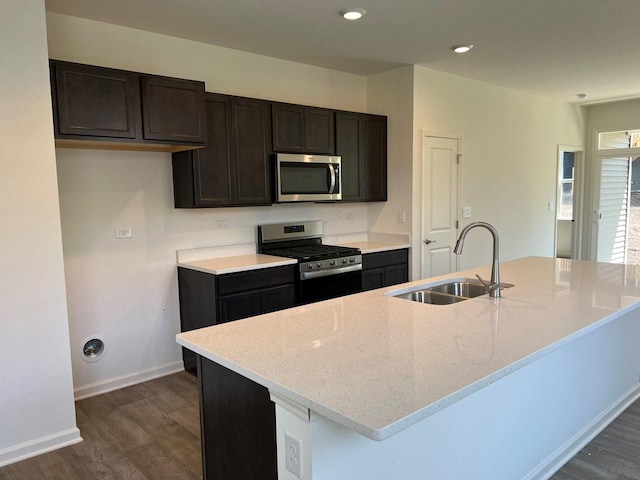 kitchen with light stone counters, sink, stainless steel appliances, and a kitchen island with sink