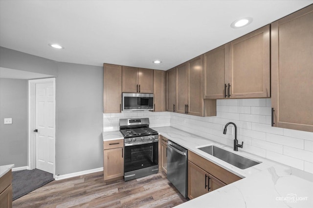 kitchen featuring hardwood / wood-style floors, backsplash, sink, light stone counters, and stainless steel appliances