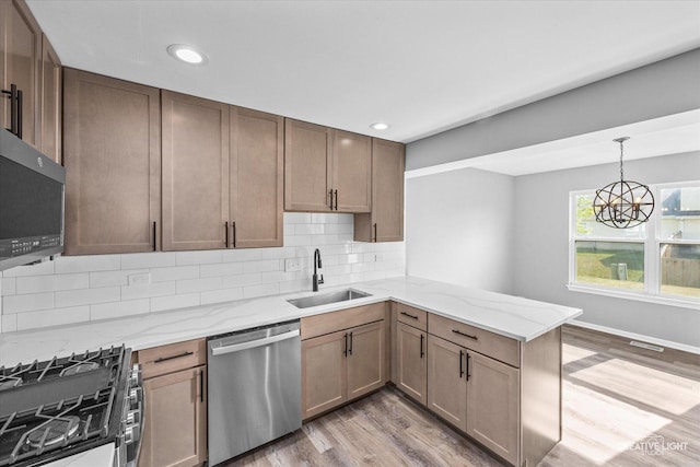 kitchen featuring kitchen peninsula, appliances with stainless steel finishes, sink, a notable chandelier, and light hardwood / wood-style floors