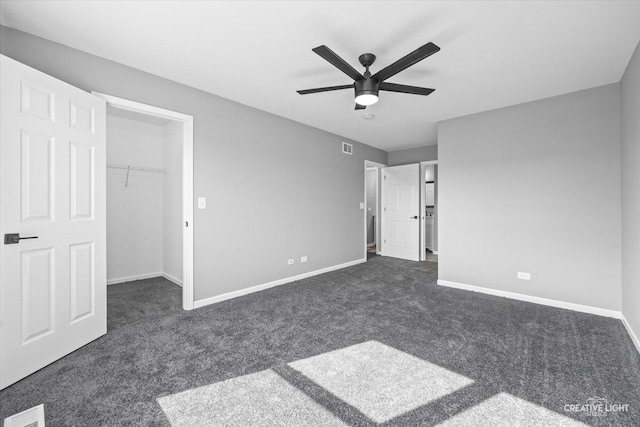 unfurnished bedroom featuring ceiling fan, dark carpet, a spacious closet, and a closet