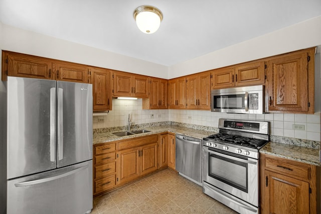 kitchen featuring tasteful backsplash, light stone counters, sink, and appliances with stainless steel finishes