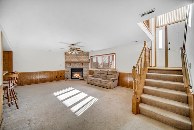 unfurnished living room with wooden walls, ceiling fan, light carpet, and a brick fireplace