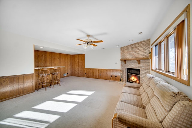 carpeted living room with a fireplace, bar area, ceiling fan, and wood walls