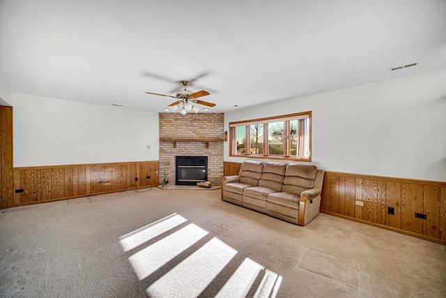 unfurnished living room with wooden walls, ceiling fan, light carpet, and a brick fireplace