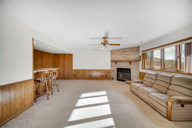 carpeted living room with bar area, a brick fireplace, ceiling fan, and wood walls