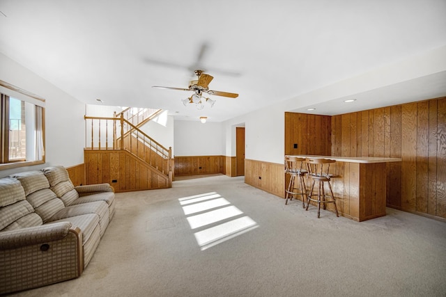 carpeted living room with ceiling fan, wood walls, and bar area