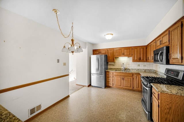 kitchen with light stone countertops, sink, stainless steel appliances, an inviting chandelier, and pendant lighting