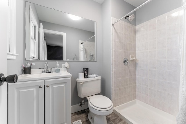 bathroom featuring a tile shower, vanity, wood-type flooring, and toilet