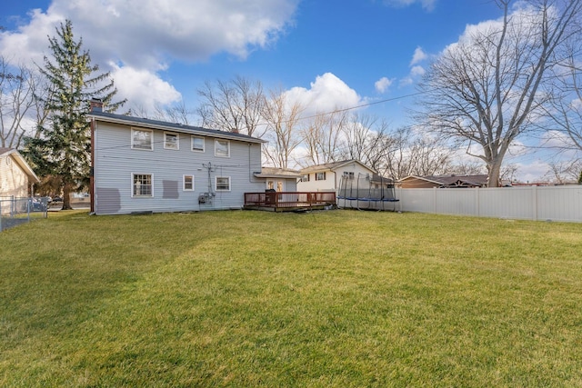 rear view of house featuring a lawn, a deck, and a trampoline