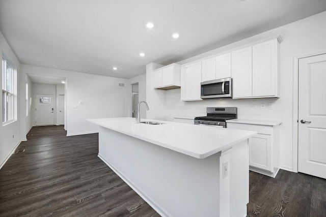 kitchen with appliances with stainless steel finishes, dark hardwood / wood-style flooring, a kitchen island with sink, sink, and white cabinetry