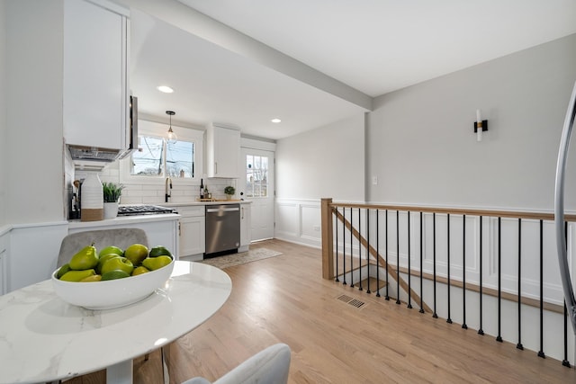 kitchen with tasteful backsplash, light hardwood / wood-style flooring, stainless steel dishwasher, pendant lighting, and white cabinets