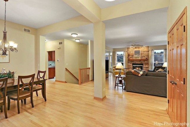 dining space with a fireplace, light hardwood / wood-style floors, and ceiling fan with notable chandelier