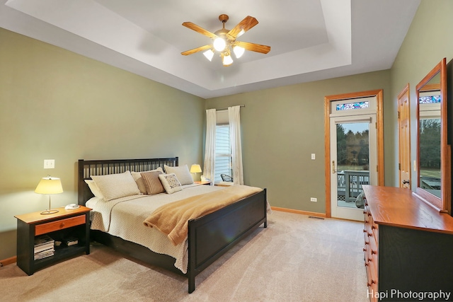 bedroom featuring a tray ceiling, multiple windows, ceiling fan, and access to outside