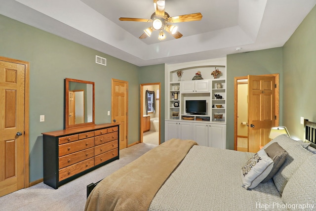 bedroom featuring light carpet, ensuite bathroom, a raised ceiling, and ceiling fan