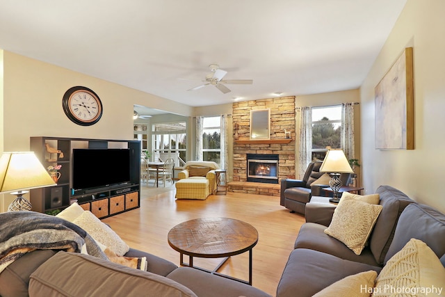 living room with a stone fireplace, ceiling fan, and light hardwood / wood-style floors