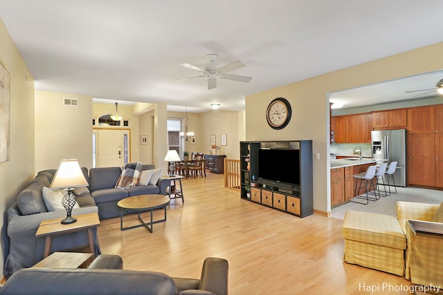 living room with sink, light hardwood / wood-style floors, and ceiling fan with notable chandelier